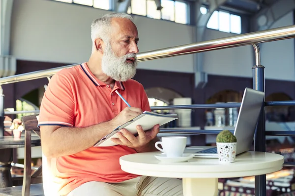 Senior schaut auf Laptop und schreibt — Stockfoto