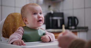 Mutlu bir kız çocuğu gülüyor ve ağzını sonuna kadar açıyor annesi de onu sandalyede kaşıkla besliyor. Zevk anlayışı, sağlıklı sütten kesme ve ebeveynlik.
