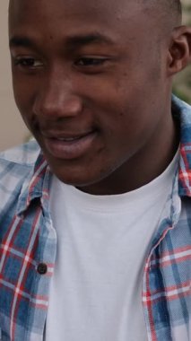 Gülümseyen genç bir Afrikalı Amerikalı kredi kartını elinde tutuyor, internetten ödeme yapmaya ya da alışveriş yapmaya hazır. Dikey video.