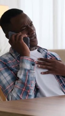 Akıllı telefonuyla gülen ve konuşan genç bir adamın dikey videosu. O, kapalı bir masada oturuyor, keyifli bir sohbetin tadını çıkarıyor..