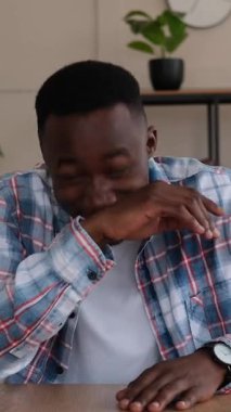 Bir video görüşmesi sırasında konuşan ve gülen, evdeki bir kupadan el kol hareketi yapan ve içki içen Afro-Amerikan bir adamın dikey videosu..