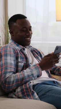 Evdeki akıllı telefonuyla konuşan ve gülen mutlu bir Afrikalı Amerikalı adamın dikey videosu..