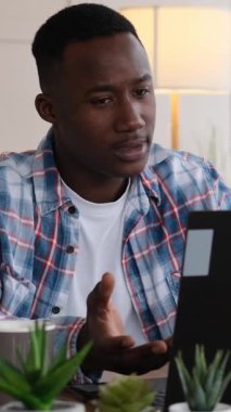 Evde bilgisayarında video görüşmesi yaparken tartışan sinirli bir Afrikalı Amerikalının dikey videosu. Stres ve hayal kırıklığı gösteriyor..