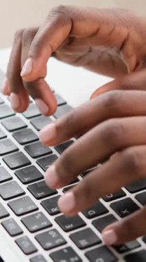 Laptop klavyesinde manikür yazan siyah bir kadının ellerine yakın çekim. Dikey video.