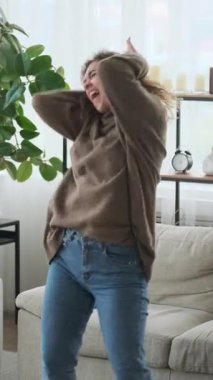 Kulaklıklı, dans eden ve oturma odasında müzik dinleyen mutlu genç bir kadının dikey videosu. Tasasız kız evde en sevdiği şarkıyla eğleniyor..