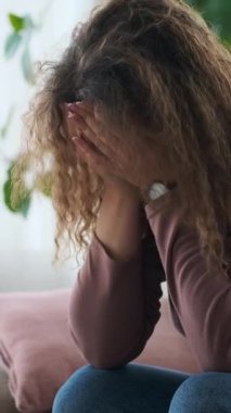 Üzgün ve depresif genç bir kadının dikey videosu. Evdeki bir kanepede oturuyor, akıl sağlığıyla ilgili sorunları var..