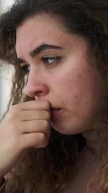 Derisi sorunlu, düşünceli ve üzgün bir genç kadının dikey videosu. Endişeli ve elleri umutsuzca yüzünü örtüyor..