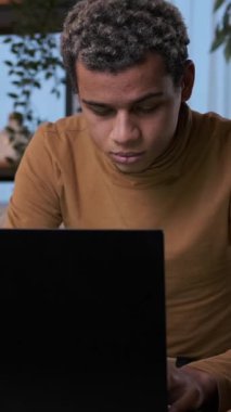 Odaklanmış genç bir adam geceleri bilgisayarında çalışır, ekrana yazar ve konsantre olur. Dikey video.