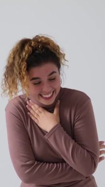 Histerik bir şekilde gülen ve beyaz bir arka planda izole edilmiş gözyaşlarını silen mutlu genç bir kadının dikey videosu. Neşeli ve olumlu duygularla dolu..