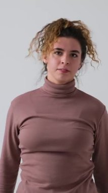 Kızgın ve hayal kırıklığına uğramış genç bir kadının beyaz bir arka planda izole edilmiş negatif duygularını ifade ettiği dikey bir video. Stresli, sinirli ve çileden çıkmış..