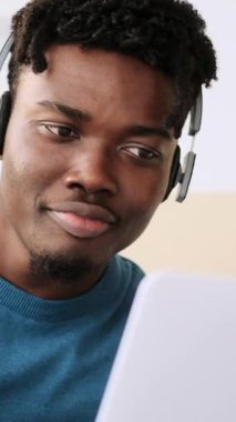 Kulaklıklı genç siyahi adam iş, ders ve eğlence için dizüstü bilgisayar kullanıyor. dikey video.