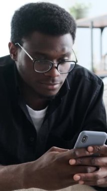 Gözlüklü, akıllı telefonunu kullanırken gülümseyen Afro-Amerikan bir adamın dikey videosu..