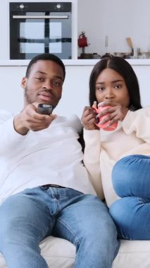 Genç siyahi bir çiftin televizyon izlediği, uzaktan kumandayla kanal değiştirdiği ve oturma odasındaki kanepede dinlenirken birlikte güldüğü dikey bir video..