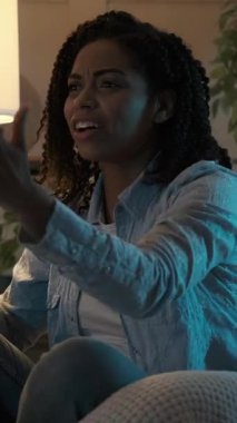 Akşamları spor maçı izleyen duygusal Afrikalı Amerikalı bir kadının dikey videosu. Heyecanlanır ve kanepede otururken takımının zaferini kutlar..