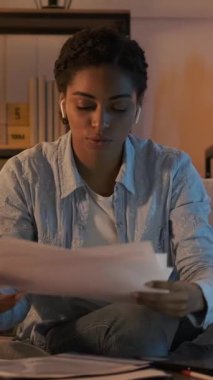 Bir video konferansında kulaklık takmış genç Afrikalı Amerikalı bir kadının dikey videosu. Geceleri kanepede oturup belgeleri inceler ve tartışır..