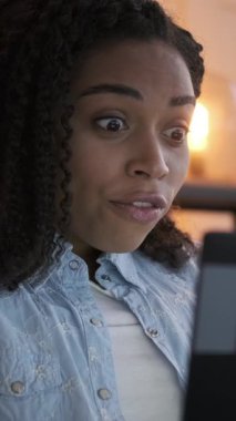 Laptop kullanan şaşırmış bir kadının dikey videosu. İnternetten heyecan verici haberler aldıktan sonra sevinçten havalara uçuyor..