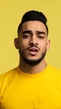Yorgun genç adam esniyor ve ağzını kapatıyor, uykulu ve sıkılmış hissediyor. Sarı arkaplanda izole edilmiş dikey video.