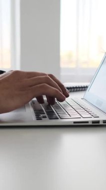 Bir adamın elleri parlak bir ofis alanında dizüstü bilgisayarda klavyeye yazı yazıyor. Dikey video.