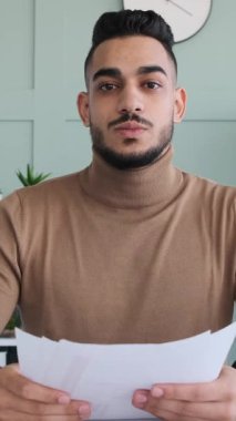 Ofisindeki bir video konferansı sırasında kameraya konuşan ve belgeleri açıklayan genç bir işadamının dikey videosu..