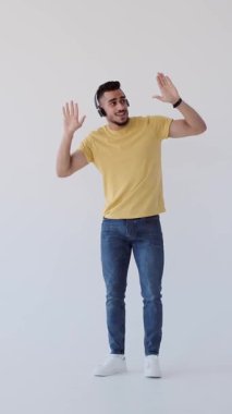 Kulaklıkla müzik dinleyen, dans eden, beyaz bir arka planda izole genç bir adamın dikey videosu..