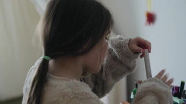 Uzun saçlı genç bir kız yatak odasındaki tutucudan rengarenk kalemler seçiyor, resim çizmeye ya da resim yapmaya hazırlanıyor..