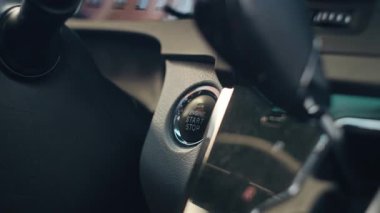 Erkek bir sürücünün parmağı modern bir arabanın kontağını çalıştırmak için motoru durdurma düğmesine basar. Arabanın iç kısmının yakın çekimi..