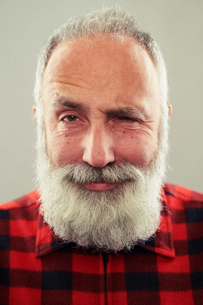 Чоловік з сіро-волохатою бородою дивиться на камеру і підморгує — стокове фото