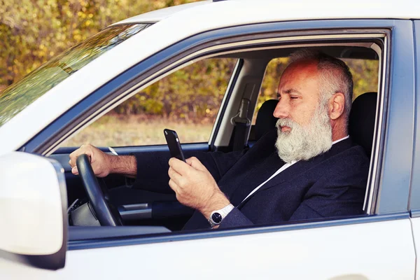 Άνθρωπος, οδηγώντας το αυτοκίνητό του και κοιτώντας στο smartphone — Φωτογραφία Αρχείου