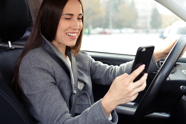 Mujer conduciendo el coche y usando su teléfono inteligente — Foto de Stock