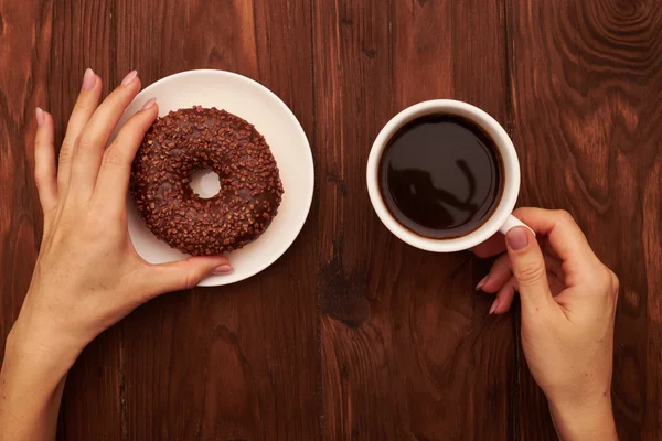 Donut de chocolate e mulheres mão com café — Fotografia de Stock