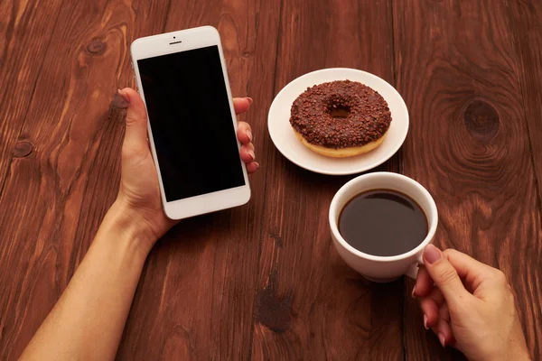 Foto de cerca de las manos de las mujeres sosteniendo el teléfono inteligente y la taza de cof — Foto de Stock