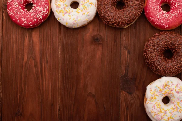 Donuts coloridos deitado sobre mesa de madeira marrom — Fotografia de Stock