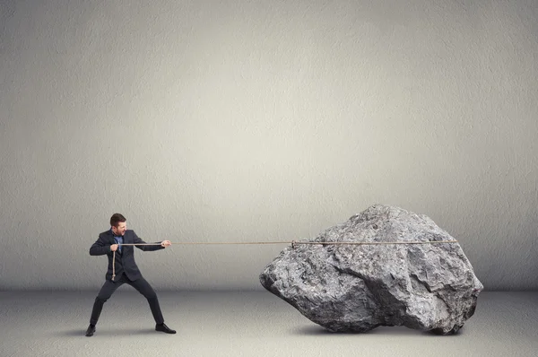 Man in formal wear pulling the big stone over light grey backgro — Stock Photo, Image