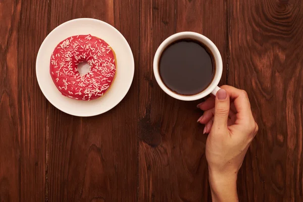 Donut rosa na placa branca e mão das mulheres — Fotografia de Stock