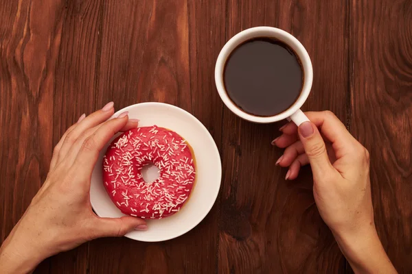 Mão mulher segurando xícara de café e donut rosa — Fotografia de Stock
