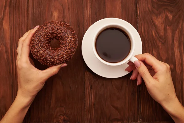Mão de mulheres com donut de chocolate e xícara de café — Fotografia de Stock