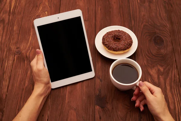 Dames handen met tablet pc en kopje koffie over bruine rug — Stockfoto