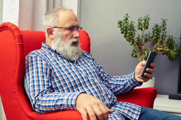 Äldre man vilar på stolen med smartphone — Stockfoto