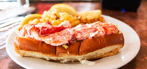 Side view of a lobster roll served with waffle fries on a white plate in a restaurant in Porland Maine.