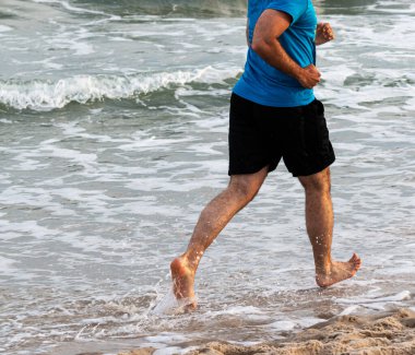New York 'taki Fire Island sahilinde yalın ayak koşan bir adamın yan görüntüsü..
