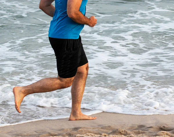 Side view of a man running barefoot on the beach next to the ocean on Fire Islands National Sea Shore during a race.