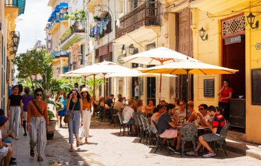 Havana, Küba - 26 Temmuz 2018: Şemsiyelerin altında turistler ve yerliler için restoranların önünde kurulmuş masalarla dolu bir sokak.