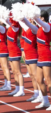 Futbol maçı boyunca taraftarlara tezahürat yaparken ponponlarını havaya kaldırmış lise ponpon kızları..