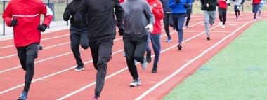 Bir liseli kış koşu takımı, bacaklarında tayt ve eşofman altı ile onları sıcak tutacak eldiven ve eşofmanlarla pistte koşuyor..