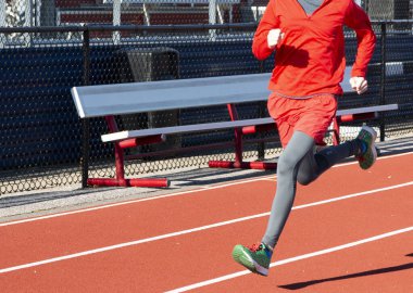 Bir liseli çocuk soğuk bir günde kırmızı bir pistte hızla koşuyor..