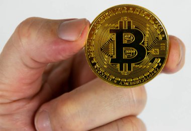 Seçici bir odak noktası olan beyaz bir arkaplan önünde altın bir bitcoin tutan bir insan elini kapat.