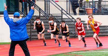 Mineola, New York, USA - 16 January 2021: A running race official in blue jacket with starting pistol in the air starting runners who are wearing face masks in an outdoor track race. clipart