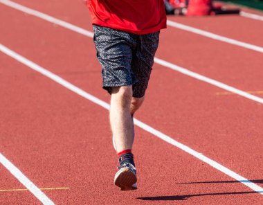 Seçici bir odak noktasıyla şeritte koşan liseli bir çocuğun alt kısmının ön tarafı bulanık bir arkaplan oluşturur..