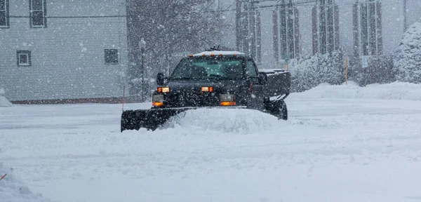 A private contracter is plowing the snow in a parking lot for the local businesses.