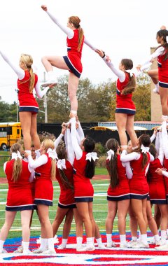 West Islip, New York, ABD - 11 Ekim 2019: Lise ponpon kızları sahanın ortasında futbol maçının yarısında tezahürat yaparken birbirlerini havaya kaldırdılar.
